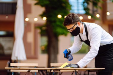 COVID-19 'u önlemek için dezenfekte ediyorum. Karantina şehrindeki kafede dezenfektan spreyi ve mikrofiber bezle koruyucu maske ve eldiven temizleme masasında garson..