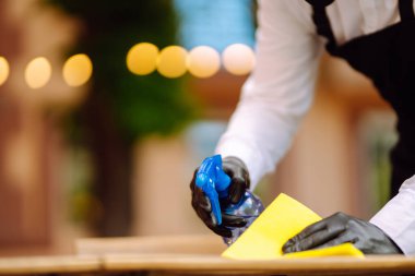 COVID-19 'u önlemek için dezenfekte ediyorum. Karantina şehrindeki kafede dezenfektan spreyi ve mikrofiber bezle koruyucu maske ve eldiven temizleme masasında garson..