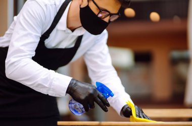 COVID-19 'u önlemek için dezenfekte ediyorum. Karantina şehrindeki kafede dezenfektan spreyi ve mikrofiber bezle koruyucu maske ve eldiven temizleme masasında garson..
