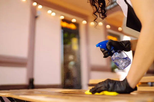 消毒以防止Covid 咖啡店的年轻女服务员戴着防护面罩 头戴手套 用消毒剂喷雾和微纤维布擦拭餐桌 — 图库照片
