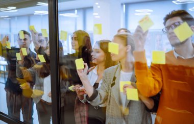 Fikirlerimizi duvar camı ofisindeki kağıt not yazma stratejisiyle paylaşıyoruz. İş adamları ofiste buluşup, fikirlerini paylaşmak için not tutuyorlar. Beyin fırtınası konsepti. Planlama, eğitim, analiz