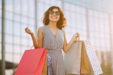 Alışverişten keyif alan neşeli bir kadın. Alışveriş torbalarıyla sokakta yürüyen modacı kadın. Tüketim, satış, alım, alışveriş, yaşam tarzı konsepti.