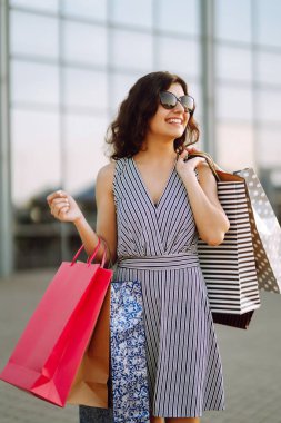 Alışverişten keyif alan neşeli bir kadın. Alışveriş torbalarıyla sokakta yürüyen modacı kadın. Tüketim, satış, alım, alışveriş, yaşam tarzı konsepti.