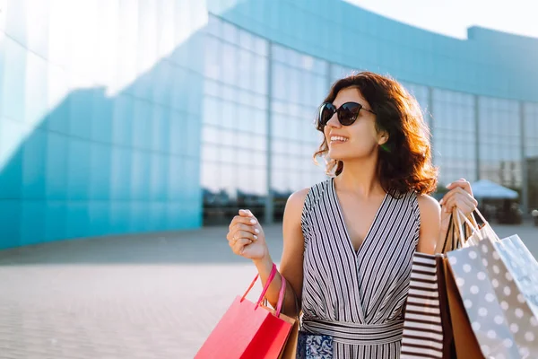 Cheerful woman enjoying shopping.  Fashion woman with shopping bags walking on street. Consumerism, sale, purchases, shopping, lifestyle concept.