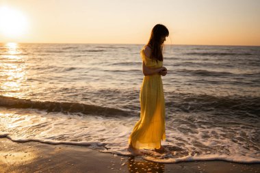 Gün batımında sahilde güzel bir kadın. Seyahat tatili boyunca açık havada huzurlu okyanus doğasının tadını çıkarıyor. Yaz zamanı..