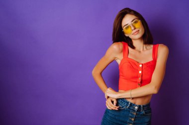 Kırmızı bluzlu, etekli, sarı gözlüklü, mor arka planda poz veren güzel bir kadın. Güzellik ve pozitif konsept.