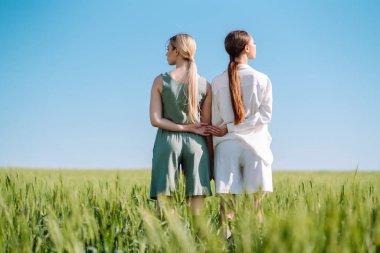 Bir tarlanın arka planında, şık ve şık giyinmiş iki sarışın kızın portresi. Doğa, tatil, rahatlama ve yaşam tarzı. Moda konsepti.