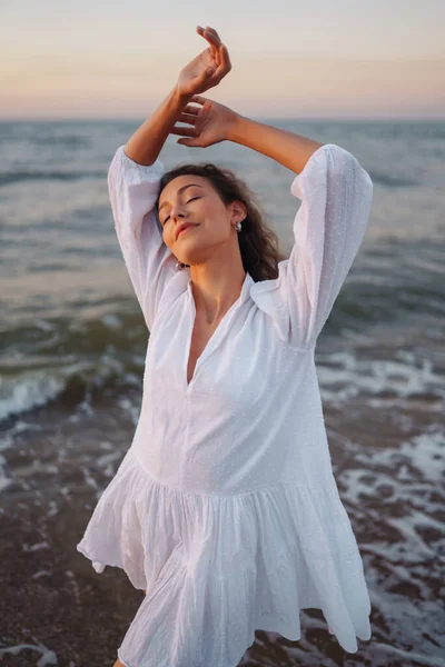 身穿白色飘扬衣服的年轻而快乐的女人沿着海滨散步 女孩看着神奇的日出 夏天的时候旅行 放松和生活方式概念 — 图库照片