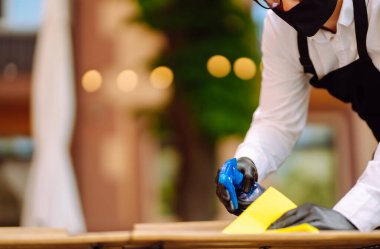 COVID-19 'u önlemek için dezenfekte ediyorum. Koruyucu yüz maskesi takan garson ve eldiven temizleme ve bir sonraki müşteri için restoran masasını dezenfekte etme.