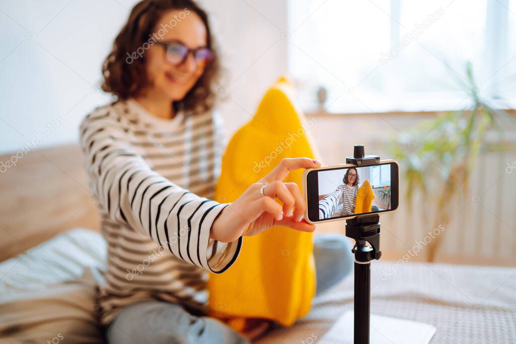 Beautiful fashion blogger holding yellow sweater dreamily recording new fashion video for vlog. Online  marketing, fashion atelier, handmade clothes.