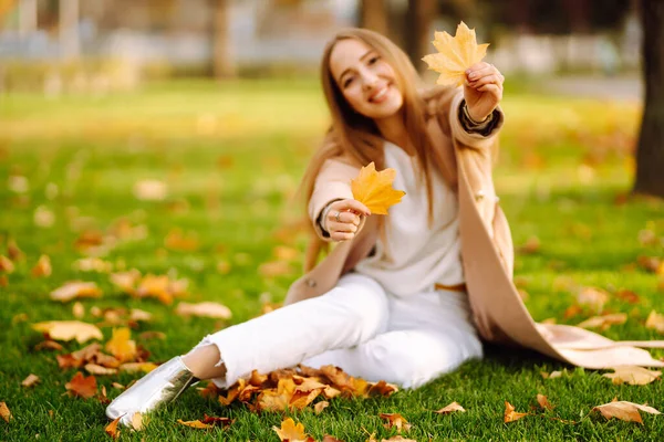 秋天阳光灿烂的日子里 一位年轻女子在公园里 面带微笑 与树叶嬉戏 秋天的时尚 生活方式 自然概念 — 图库照片