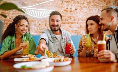 Mutlu arkadaşlar kafede harika vakit geçiriyorlar. Gençler restoranda oturup eğleniyorlar, gülüyorlar, kokteyl içiyorlar ve yemek yiyorlar. Dostça bir yemek..
