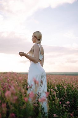 Güzel romantik kız gün batımında dışarıda. Tarlada poz veren şık giyinmiş genç bir kadın. Doğa, tatil, rahatlama ve yaşam tarzı. Moda konsepti.