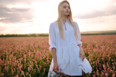 Güzel romantik kız gün batımında dışarıda. Tarlada poz veren şık giyinmiş genç bir kadın. Doğa, tatil, rahatlama ve yaşam tarzı. Moda konsepti.