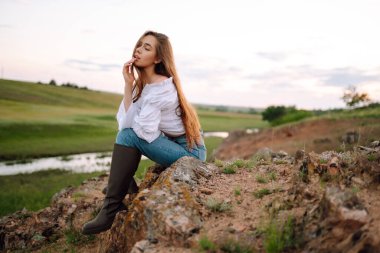 Kırsalda poz veren kovboy çizmeleri giyen neşeli genç bir kadın. Moda, tarz, yaşam tarzı konsepti. Yaz zamanı..