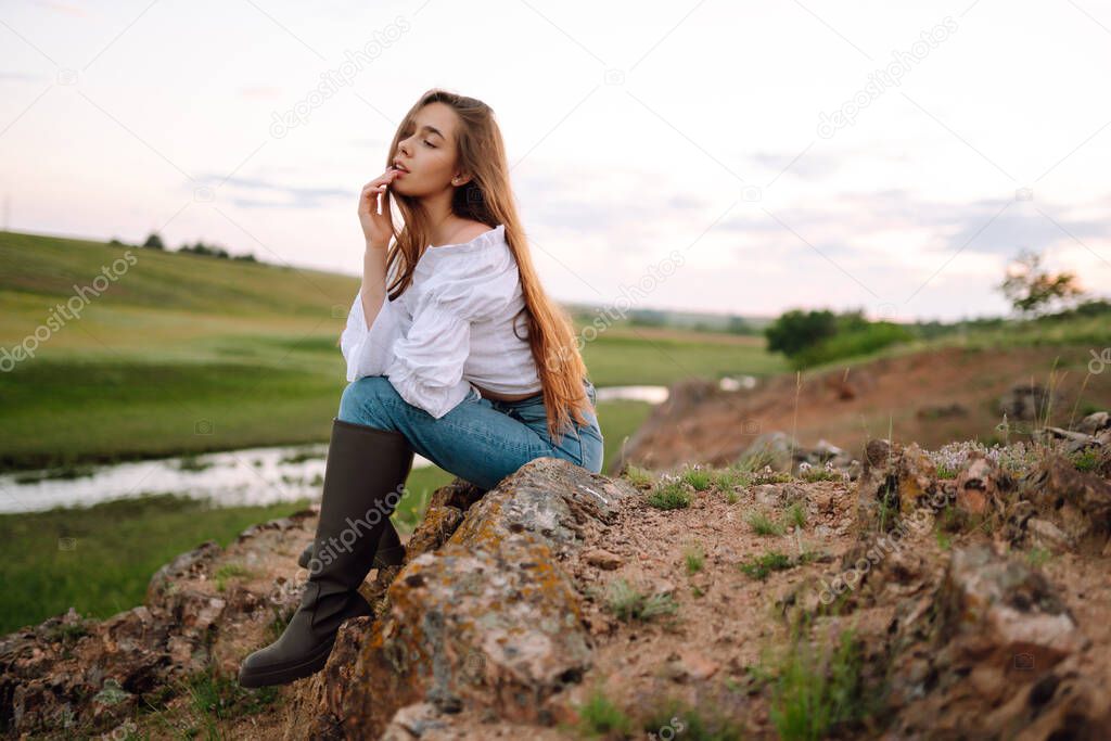 Young cheerful woman wearing cowgirl boots posing in the countryside. Fashion, style, lifestyle concept. Summer time.