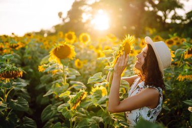 Gün batımında elinde ayçiçekleriyle tarlada gezinen güzel bir kadın. Kırsal ve mutlu bir hayat. Doğa, rahatla ve yaşam tarzı.