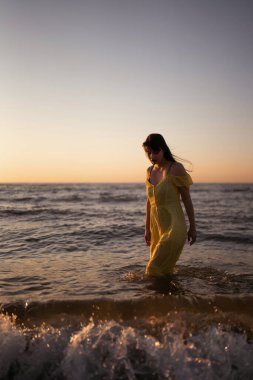 Genç bir kadın gün batımında deniz kıyısında yürüyor. Doğa, rahatla, yaşam tarzı konsepti.