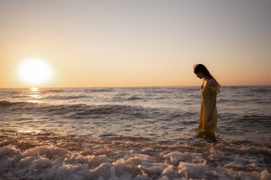 Genç bir kadın gün batımında deniz kıyısında yürüyor. Doğa, rahatla, yaşam tarzı konsepti.