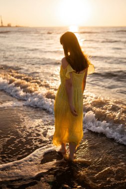 Genç bir kadın gün batımında deniz kıyısında yürüyor. Doğa, rahatla, yaşam tarzı konsepti.