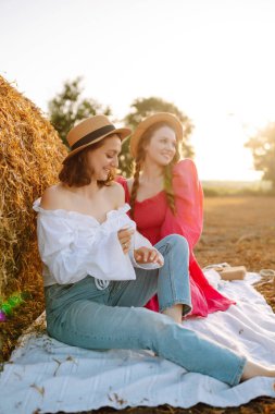 Two smiling young woman resting near haystack. Fashion concept. Nature, vacation, relax and lifestyle.