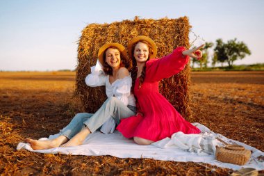 Two smiling young woman resting near haystack. Fashion concept. Nature, vacation, relax and lifestyle.