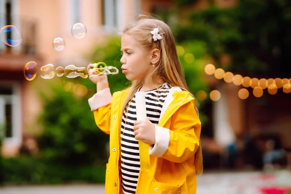 Little Girl Yellow Cloak Rubber Boots Blowing Soap Bubbles Outdoors — Stockfoto
