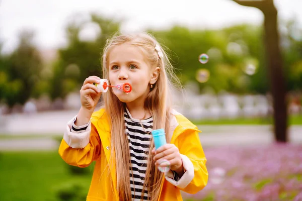 Little Girl Yellow Cloak Rubber Boots Blowing Soap Bubbles Outdoors — Fotografia de Stock