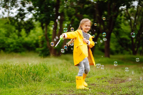 Little Girl Yellow Cloak Rubber Boots Blowing Soap Bubbles Outdoors — Stockfoto