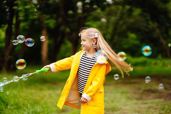 Little Girl Yellow Cloak Rubber Boots Blowing Soap Bubbles Outdoors — Stockfoto