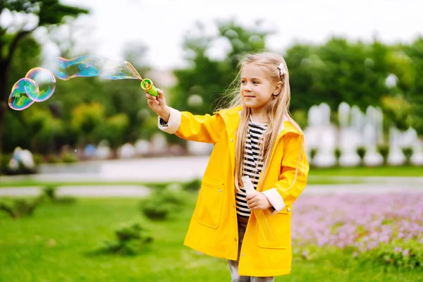 Little Girl Yellow Cloak Rubber Boots Blowing Soap Bubbles Outdoors — Fotografia de Stock