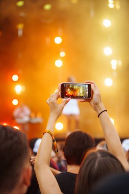 Using a smartphone in a public event,  live music festival.  Holding a mobile phone in hands and shooting photo or video content.  Youth, party, vacation concept.