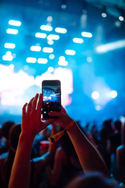 Using a smartphone in a public event,  live music festival.  Holding a mobile phone in hands and shooting photo or video content.  Youth, party, vacation concept.