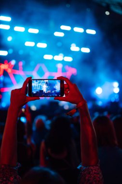 Using a smartphone in a public event,  live music festival.  Holding a mobile phone in hands and shooting photo or video content.  Youth, party, vacation concept.