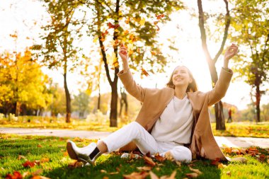 Young woman having fun throwing leaves in autumn at city park. Lifestyle. Relax, nature concept. Autumn mood concept.