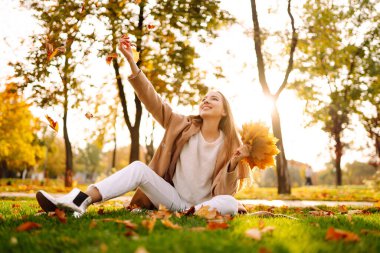 Young woman having fun throwing leaves in autumn at city park. Lifestyle. Relax, nature concept. Autumn mood concept.