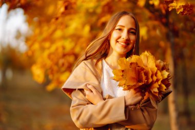 Young woman having fun throwing leaves in autumn at city park. Lifestyle. Relax, nature concept. Autumn mood concept.