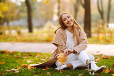 Young woman having fun throwing leaves in autumn at city park. Lifestyle. Relax, nature concept. Autumn mood concept.