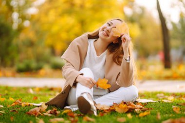 Young woman having fun throwing leaves in autumn at city park. Lifestyle. Relax, nature concept. Autumn mood concept.