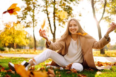 Young woman having fun throwing leaves in autumn at city park. Lifestyle. Relax, nature concept. Autumn mood concept.