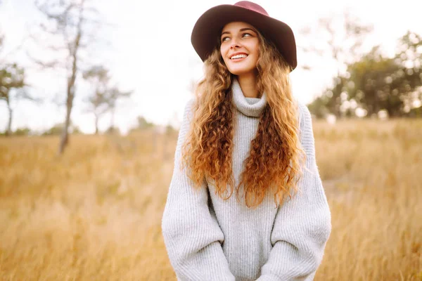 Stylish woman in sweater and hat enjoys autumn nature. People, freedom, lifestyle, travel and vacations concept.