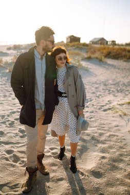 Genç çift, sonbahar güneşli günlerinde kumsalda yürüyüp sarılıyor. Rahatlama, gençlik, aşk, doğayla baş başa yaşam tarzı.