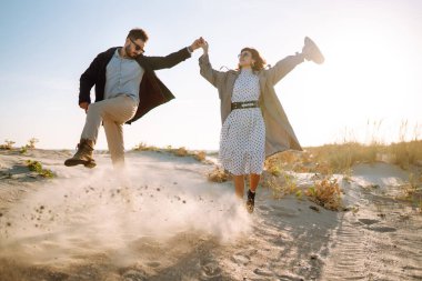 Genç çift, sonbahar güneşli günlerinde kumsalda yürüyüp sarılıyor. Rahatlama, gençlik, aşk, doğayla baş başa yaşam tarzı.