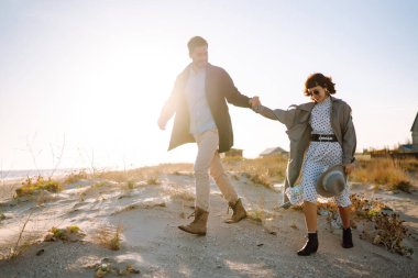 Genç çift, sonbahar güneşli günlerinde kumsalda yürüyüp sarılıyor. Rahatlama, gençlik, aşk, doğayla baş başa yaşam tarzı.