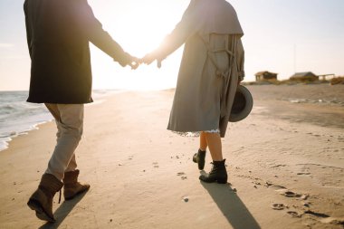 Genç çift, sonbahar güneşli günlerinde kumsalda yürüyüp sarılıyor. Rahatlama, gençlik, aşk, doğayla baş başa yaşam tarzı.