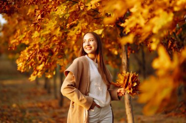 Mutlu kadın parkta sonbahar sarısı yapraklarıyla oynayıp eğleniyor. Yaşam tarzı. Rahatla, doğa konsepti. Sonbahar stili.