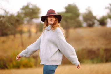 Kazaklı ve şapkalı genç bir kadın parkta sonbahar gününün tadını çıkarıyor. Moda, tarz kavramı.