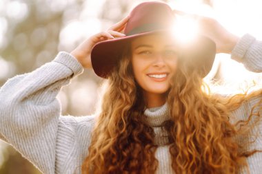 Kazaklı ve şapkalı genç bir kadın parkta sonbahar gününün tadını çıkarıyor. Moda, tarz kavramı.