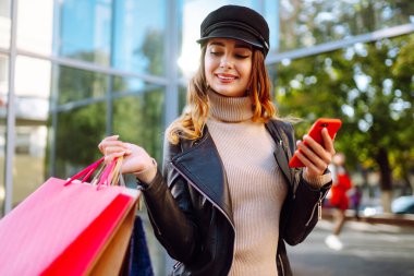Telefonla alışveriş yapan genç bir kadın. Sonbahar tarzı. İnternetten alışveriş konsepti. Satın almalar, Kara Cuma, indirimler, satış konsepti. 