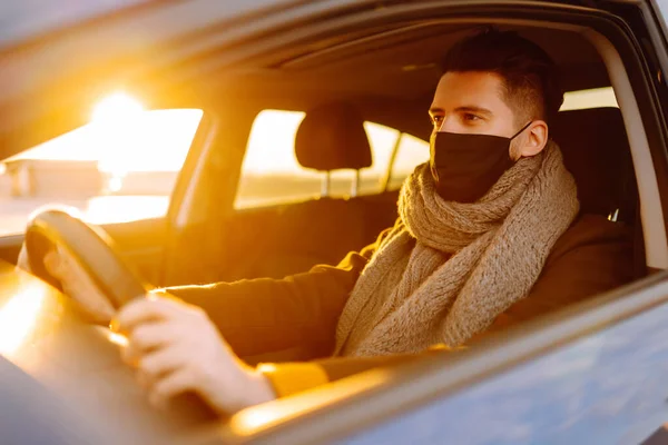 Man driving a car wearing on a medical mask during an epidemic, a driver in a mask, protection from the virus. Transport isolation. Covid-2019.